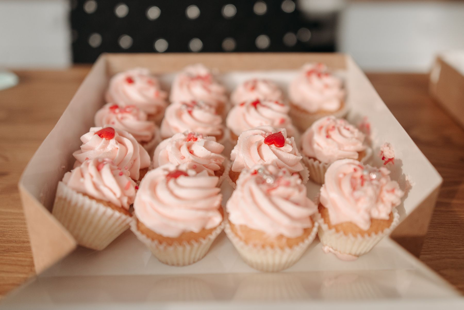 A box of pink buttercream cupcakes decorated with little red hearts