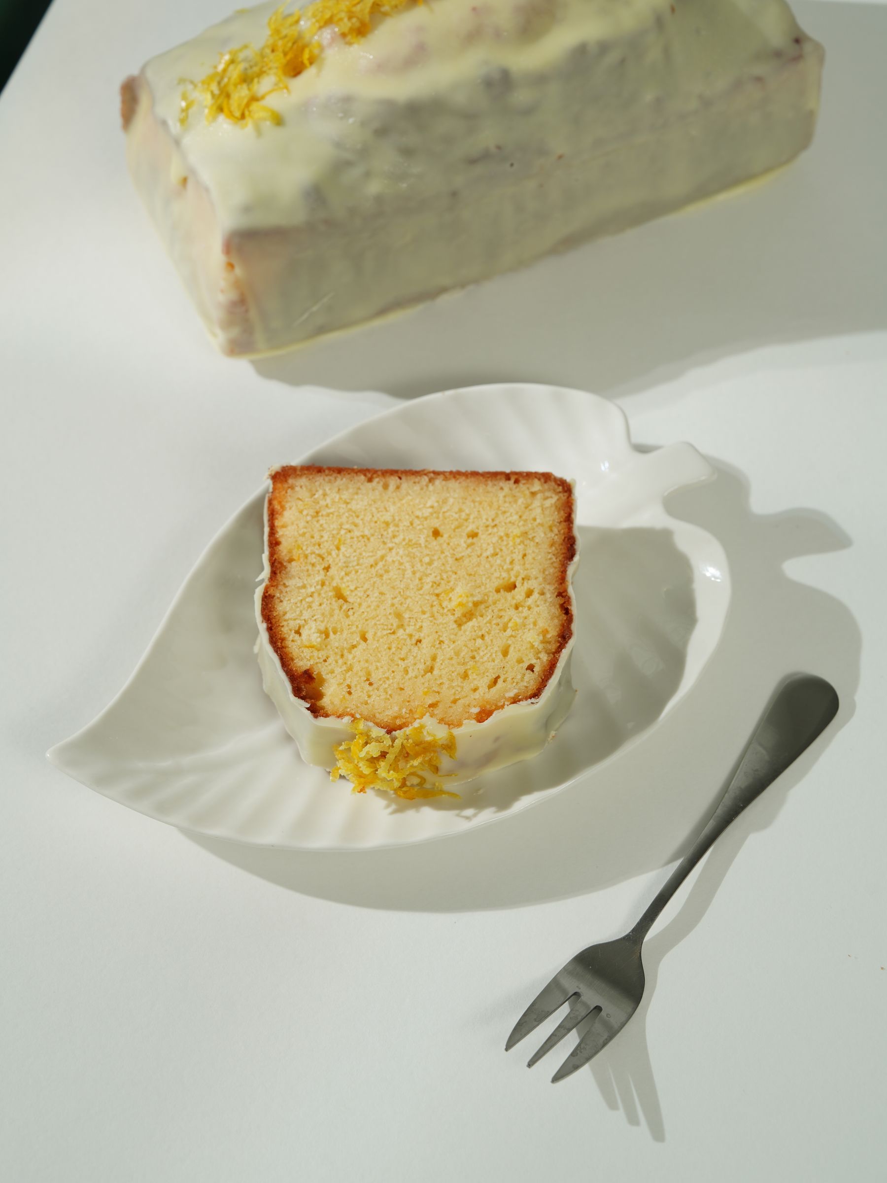Glazed lemon loaf and a golden slice on a white plate